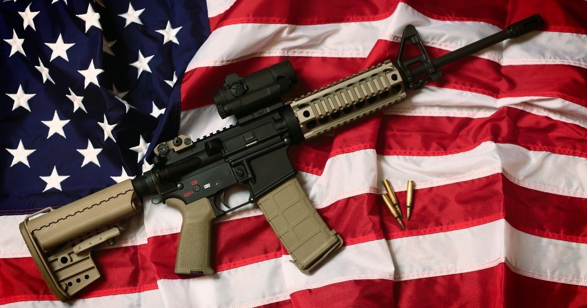 The above stock photo shows an AR-15 rifle with bullets on an American flag, a symbol of the right of patriotic Americans to bear arms, guaranteed by the Second Amendment.
