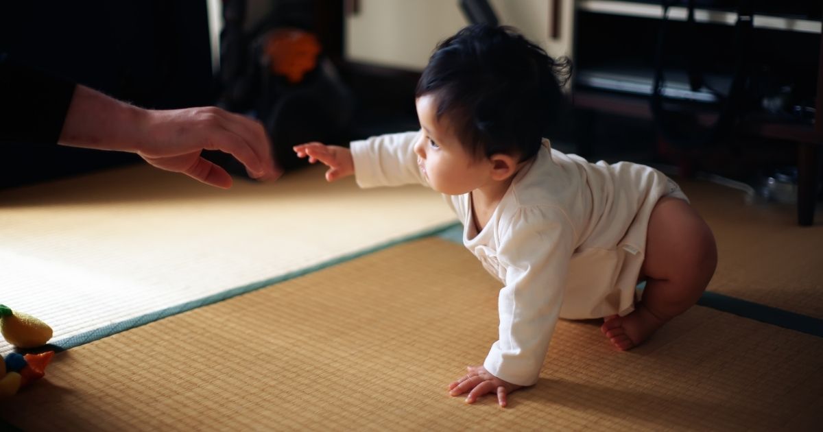 In this stock photo, a baby crawls toward an outstretched hand, ready to stand up.