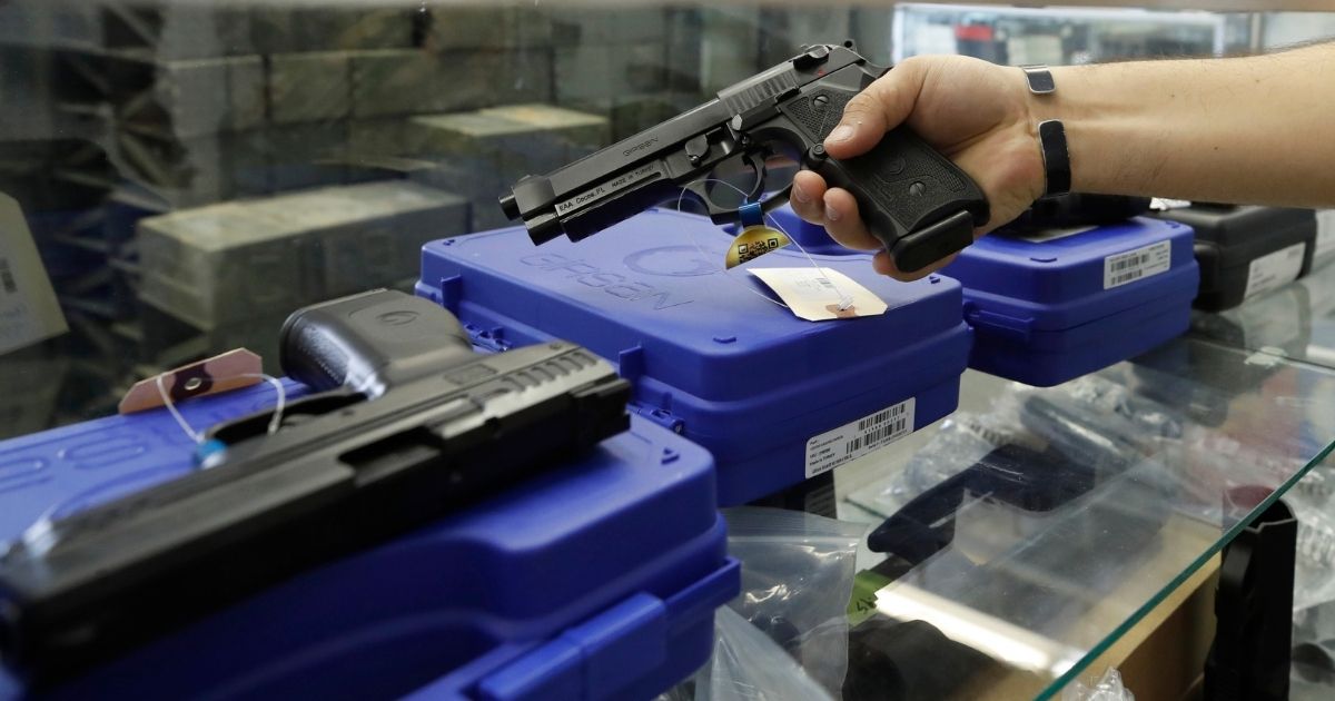 A worker pulls a handgun out of the case for a customer at Davidson Defense in Orem, Utah, on Feb. 4, 2021.