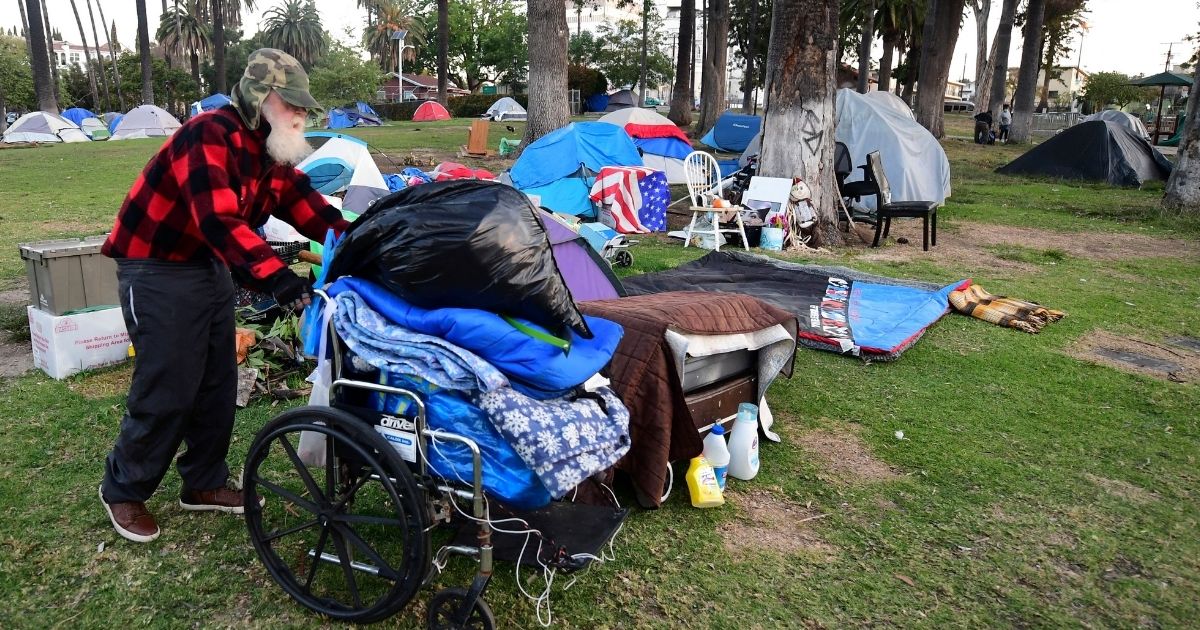 A man pushes his belongings at a homeless encampment at Echo Park Lake in Los Angeles on March 24.
