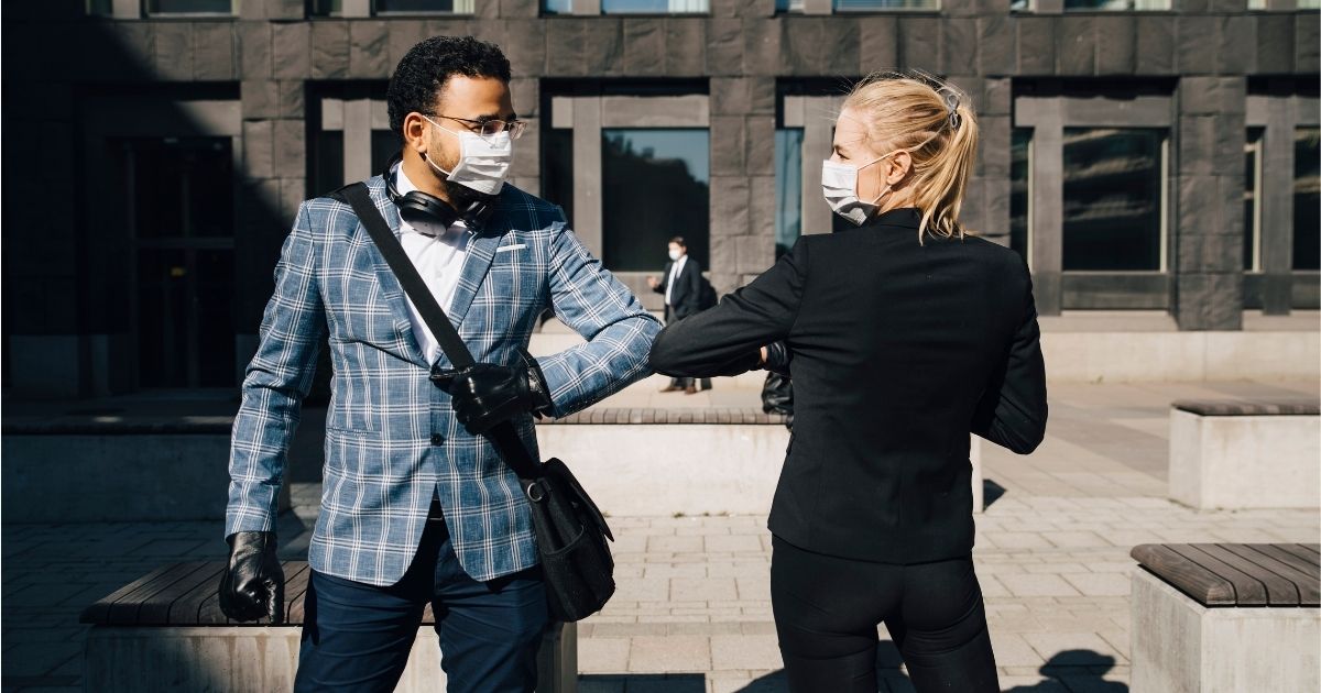 In this stock photo, a man and woman wear masks while interacting outside.
