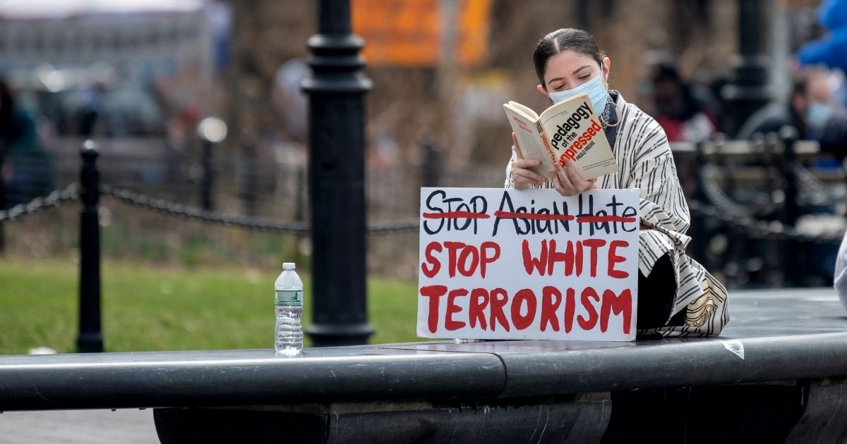A woman reading a book sits with a a "stop Asian Hate, stop white terrorism" sign in Washington Square Park on March 25, 2021, in New York City.
