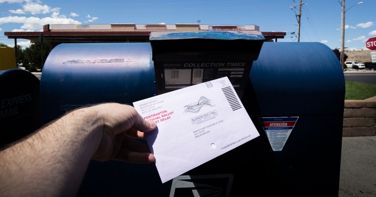 A man places a ballot in a mailbox in the above stock image.