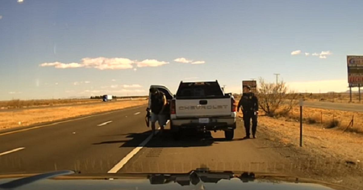 A New Mexico State Police officer stands on the passegenger side of a pickup truck as a man gets out of the vehicle on the driver's side.