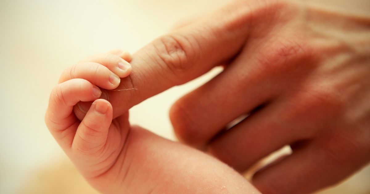 A newborn baby grasps a woman's finger in the above stock image.