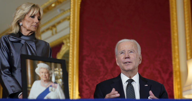 President Joe Biden, right, sits down to sign an official condolence book for Queen Elizabeth II at Lancaster House in London on Sunday.