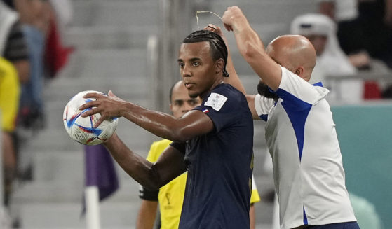 An assistant coach takes off the necklace of France's Jules Kounde during the World Cup soccer match between France and Poland at the Al Thumama Stadium in Doha, Qatar, on Sunday.