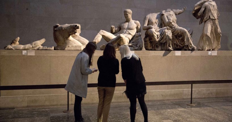 Women stand by a marble statue thought to represent Greek god Dionysos, center, from the east pediment of the Parthenon, during a media photo opportunity to promote an event at the British Museum in London, on Jan. 8, 2015.