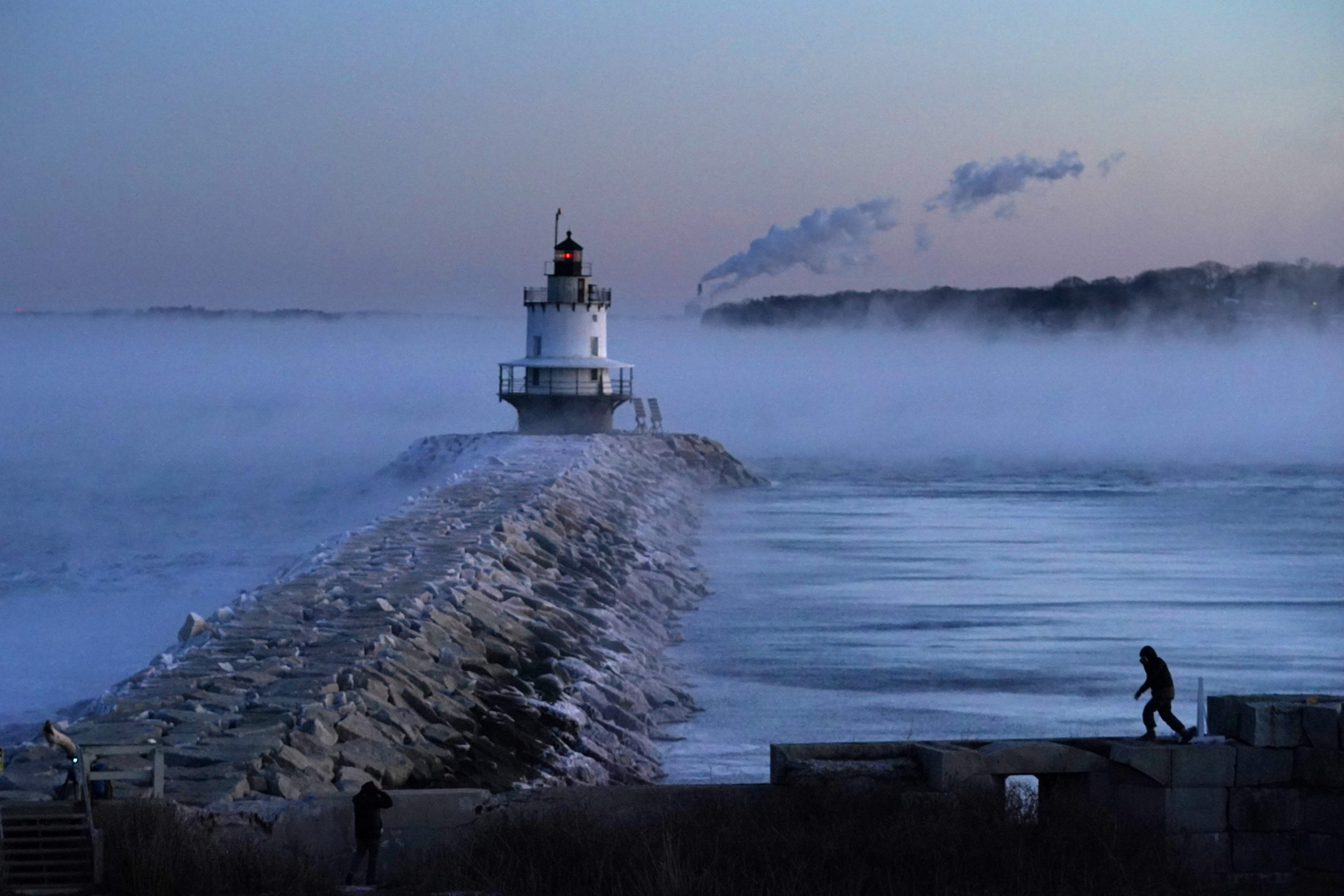 A man walks on a sea wall near Spring Point Ledge Light in South Portland, Maine, on Saturday. Morning temperatures there hovered near 10 below zero.