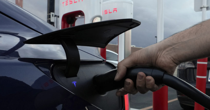 A man plugs in his electric vehicle at a Tesla Supercharger in Detroit, Michigan, on Nov. 16, 2022.