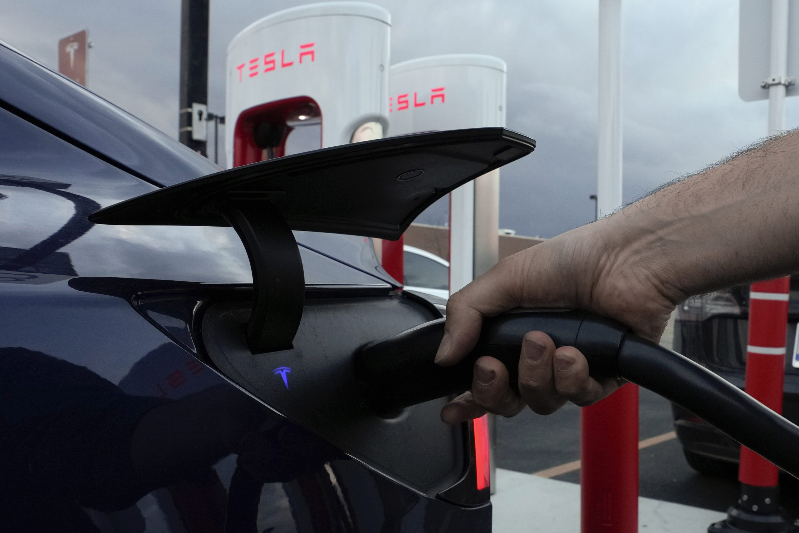 A man plugs in his electric vehicle at a Tesla Supercharger in Detroit, Michigan, on Nov. 16, 2022.