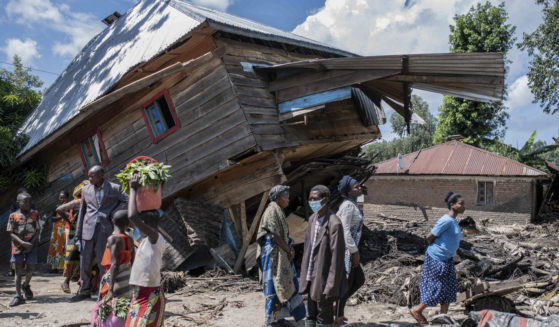 People walk next to a house destroyed by the floods in the village of Nyamukub, Congo, on Sunday.