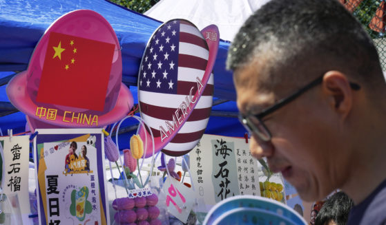 A man walks by a booth selling foods and beverages displaying planet-shaped flags of China and the U.S. during a spring carnival in Beijing on May 13. China has detained a worker from a military group on suspicion of spying for the CIA.