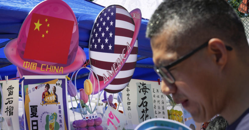 A man walks by a booth selling foods and beverages displaying planet-shaped flags of China and the U.S. during a spring carnival in Beijing on May 13. China has detained a worker from a military group on suspicion of spying for the CIA.