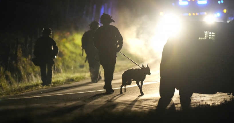 A member of law enforcement walks with a police dog outside a property on Meadow Road in Bowdoin, Maine, on Oct. 26.