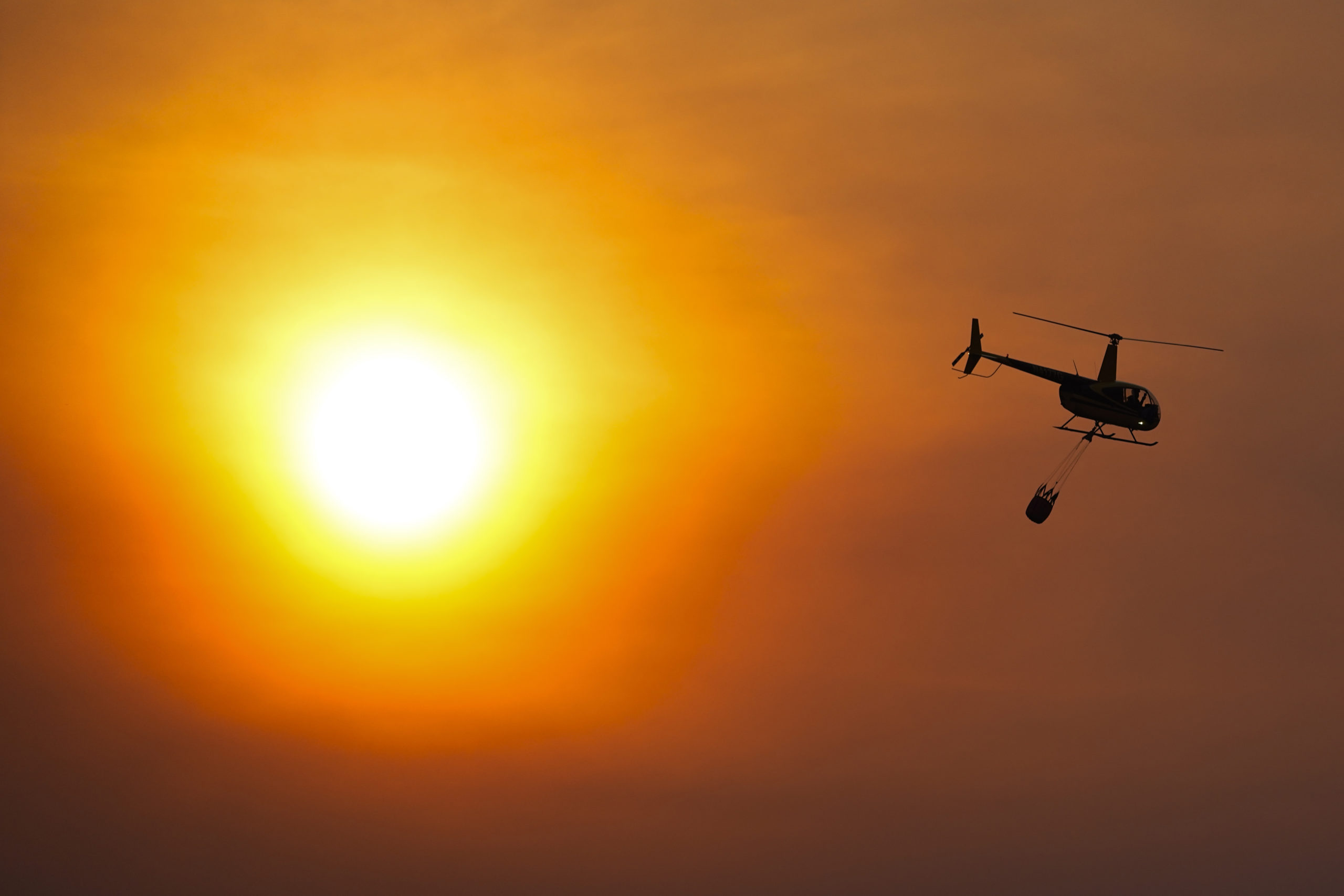 A helicopter carries a water bucket as it flies over homes burned by the Smokehouse Creek Fire Feb. 28 in Canadian, Texas.