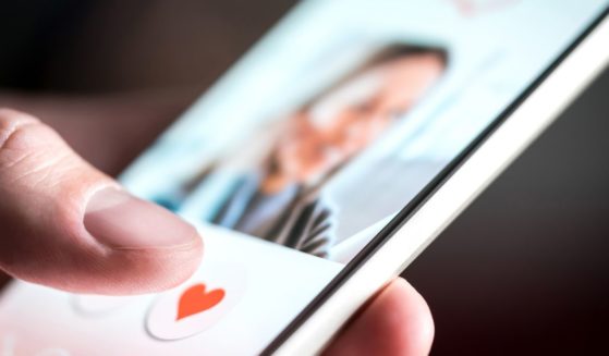 This image shows a young man's hand as he is swiping and liking profiles on a relationship site.