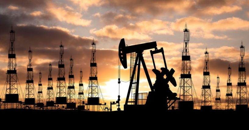 An oil field with rigs is photographed at sunset.