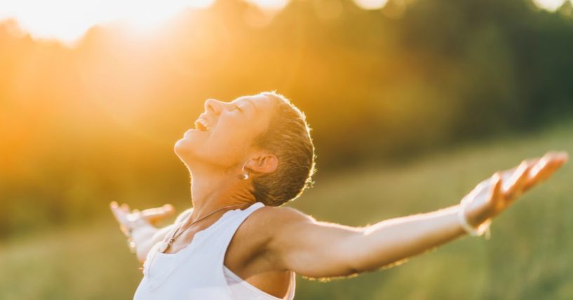 This image shows a woman outside with arms opened wide and the sunlight on her face.