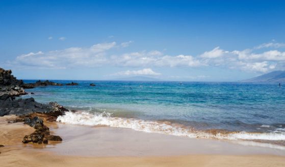 On a sunny day at Wailea beach, small waves break on the sand near volcanic rocks as tourists snorkel and use stand up paddleboards, Wailea, Maui, Hawaii, 2016.