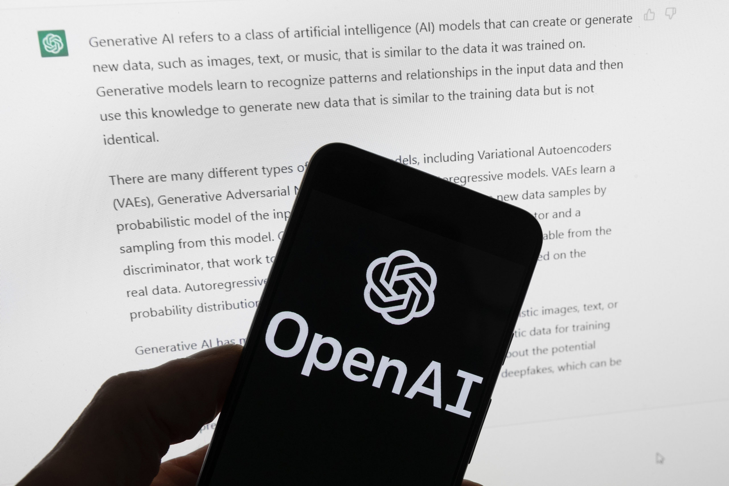 The Open AI logo is seen on a mobile phone in front of a computer screen displaying output from the company's ChatGPT software in Boston on March 21, 2023.