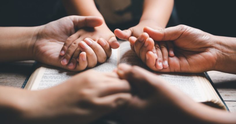 A mother and father and child holding hands in prayer over the family Bible.