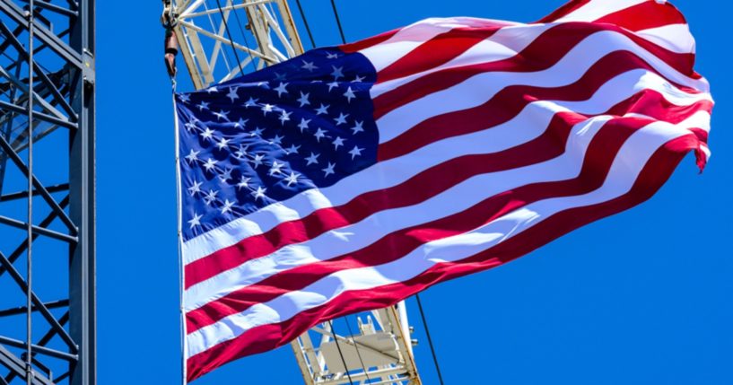 The American flag waves proudly from construction cranes under a brilliant blue sky.