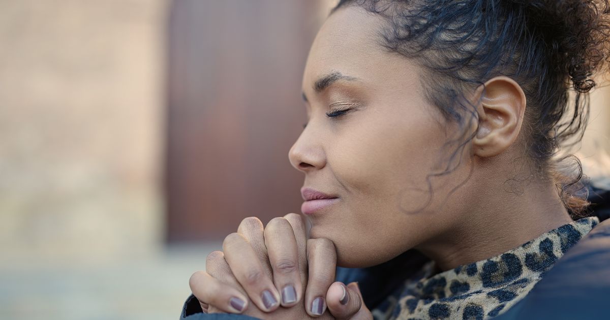 This image is a close up of a woman praying with her eyes closed and her hands interlocked and drawn toward her chin. She seems to be at peace.
