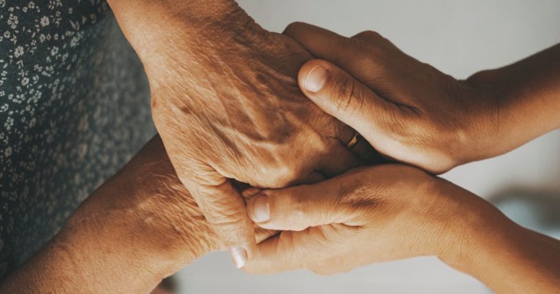 This image shows the hands of an elderly woman being held by those of a younger adult.