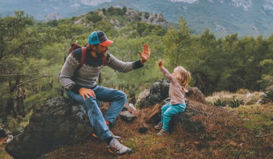 A father and daughter high-five in the mountains after hiking together.