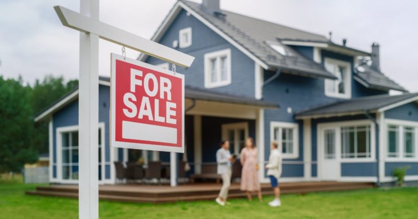 a young couple talking with a real estate agent outside a home for sale