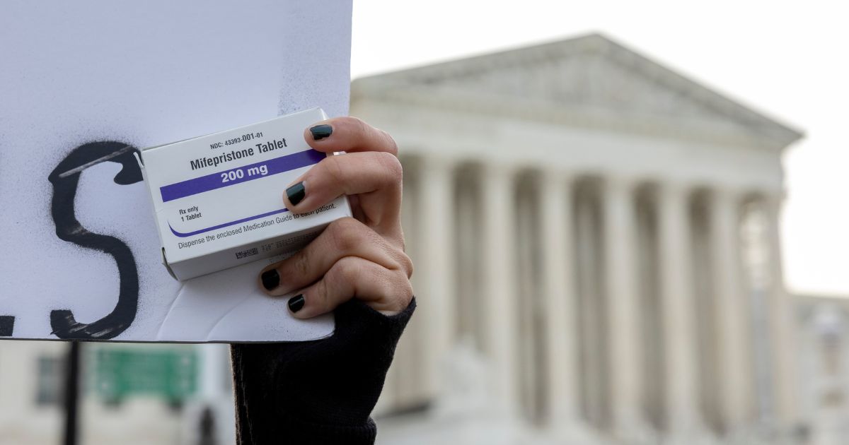 A pro-abortion activist holds a box of mifepristone pills while demonstrating outside the U.S. Supreme Court in Washington, D.C., on March 26.